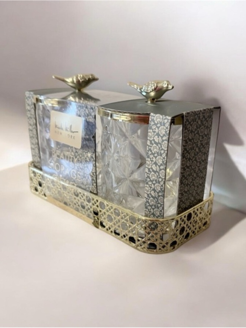two-piece glass storage jar set with a gold bird lid and decorative tray.